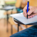 A man is writing/signing on a paper. Focused on a hand with pen
