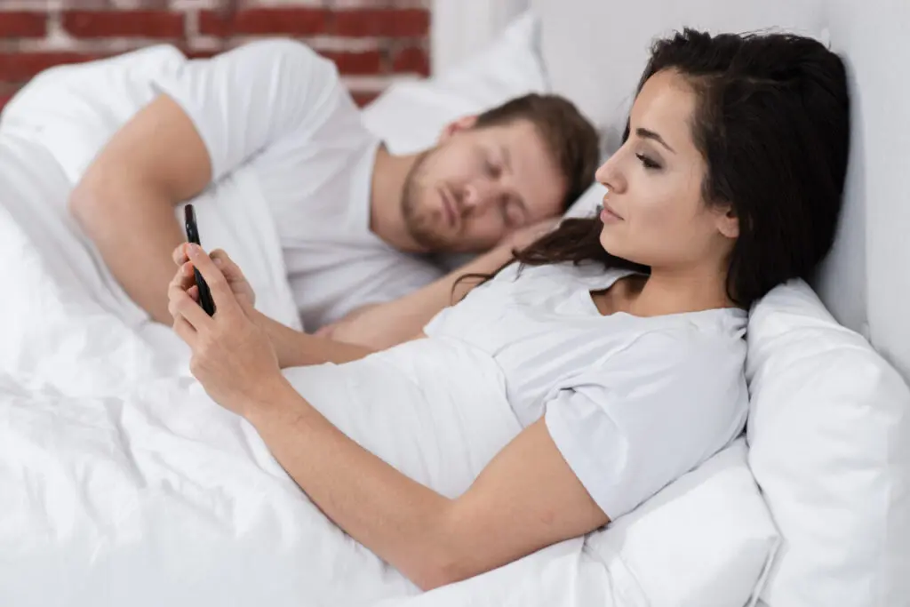 vista-lateral-mulher-verificando-seu-telefone-ao-lado-do-namorado-dormindo