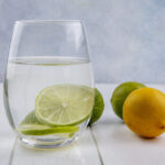 front view water in a glass with lime and lemon on a white background