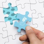 close-up-human-hand-holding-blue-puzzle-piece-with-brain-cogwheel-drawing