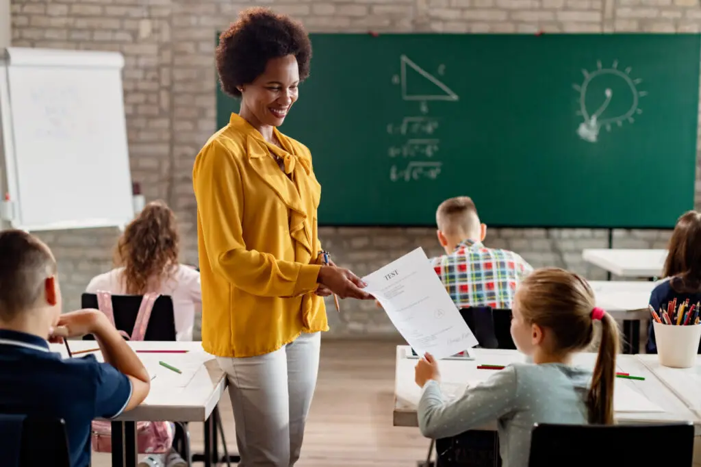 Happy African American teacher giving test results to elementary