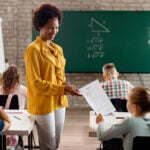 Happy African American teacher giving test results to elementary