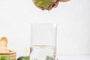 side view of female hand squeezing fresh lemon into a glass of water on white background