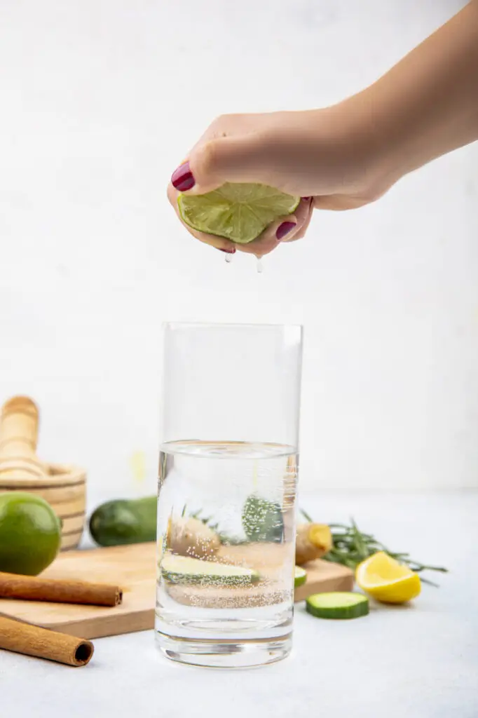 side view of female hand squeezing fresh lemon into a glass of water on white background