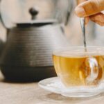 bule-e-xicara-de-cha-quente-em-uma-mesa-mao-segurando-uma-colher-de-cha_1157-48979