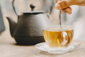 bule-e-xicara-de-cha-quente-em-uma-mesa-mao-segurando-uma-colher-de-cha_1157-48979