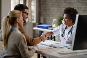 Happy African American doctor greeting a couple at medical clini