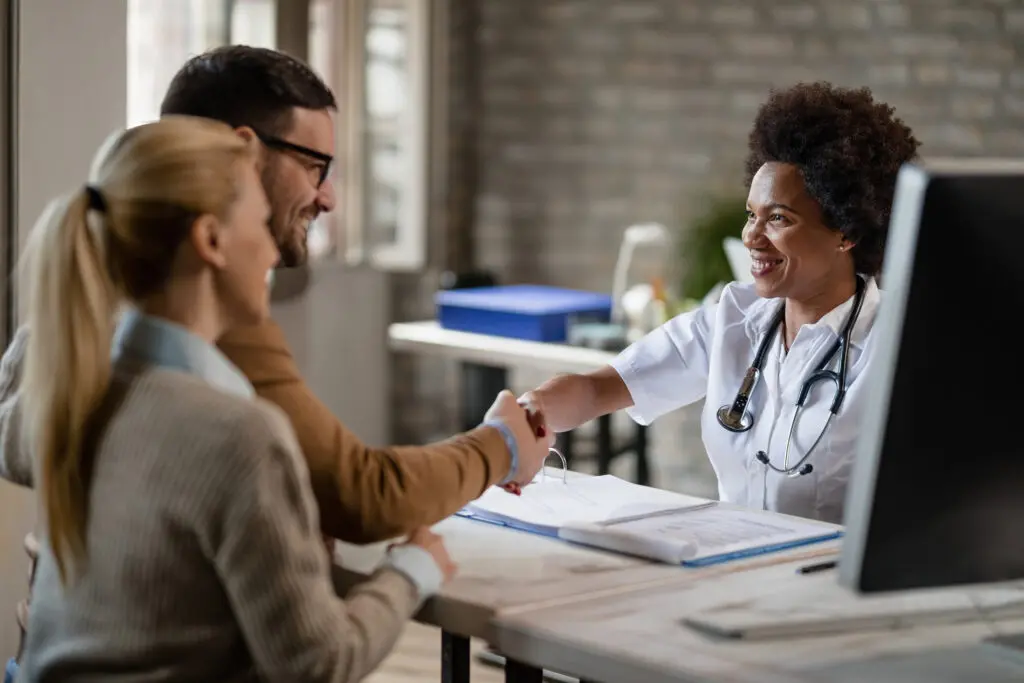 Happy African American doctor greeting a couple at medical clini