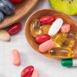 Closeup shot of fresh fruits with different medicine on a wooden spoon