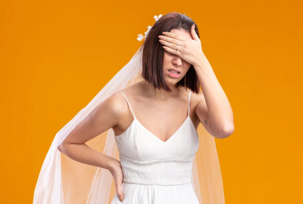 bride in beautiful wedding dress looking unwell covering eyes with hand standing over orange background