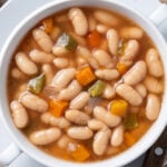 White beans soup with vegetables in white bowl on wooden table