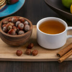 front view hazelnut in a bowl with a cup of tea and cinnamon on a board on a wooden background