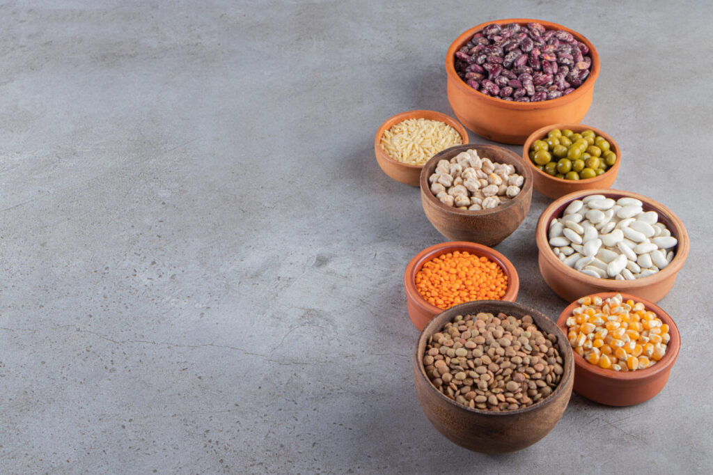 Clay bowls full of raw lentil, peas and beans on stone background
