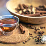 Cup of freshly brewed black tea, different types of spices on wooden table.