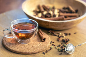 Cup of freshly brewed black tea, different types of spices on wooden table.