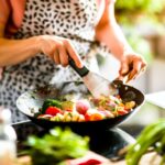 A woman in her kitchen, surrounded by fresh ingredients, expertly flips vegetables in a wok for a delicious stir fry.