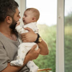 vista-lateral-pai-segurando-bebe-em-casa