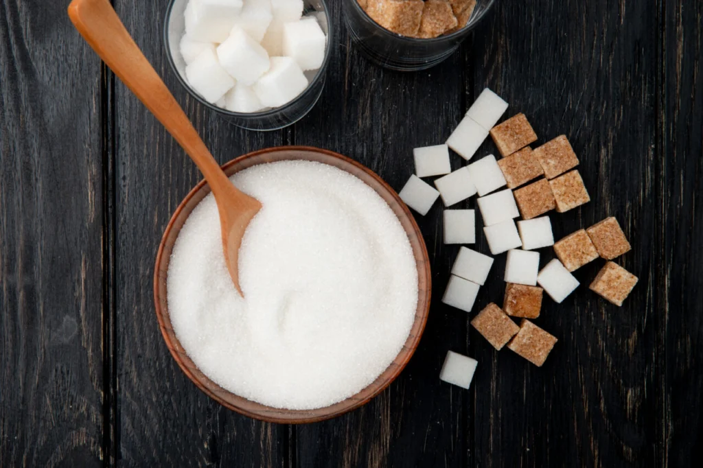 top view of different types and forms of sugar in a bowl and glasses on black wooden background