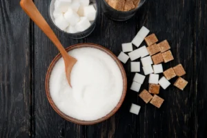 top view of different types and forms of sugar in a bowl and glasses on black wooden background