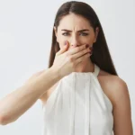 displeased-young-brunette-girl-covering-mouth-with-hand-white-backround