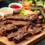 lamb steak pieces with sauces, grilled pepper, fresh salad on wooden board
