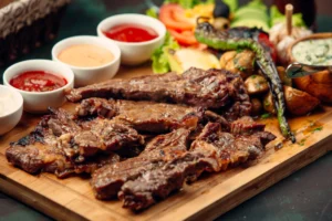 lamb steak pieces with sauces, grilled pepper, fresh salad on wooden board